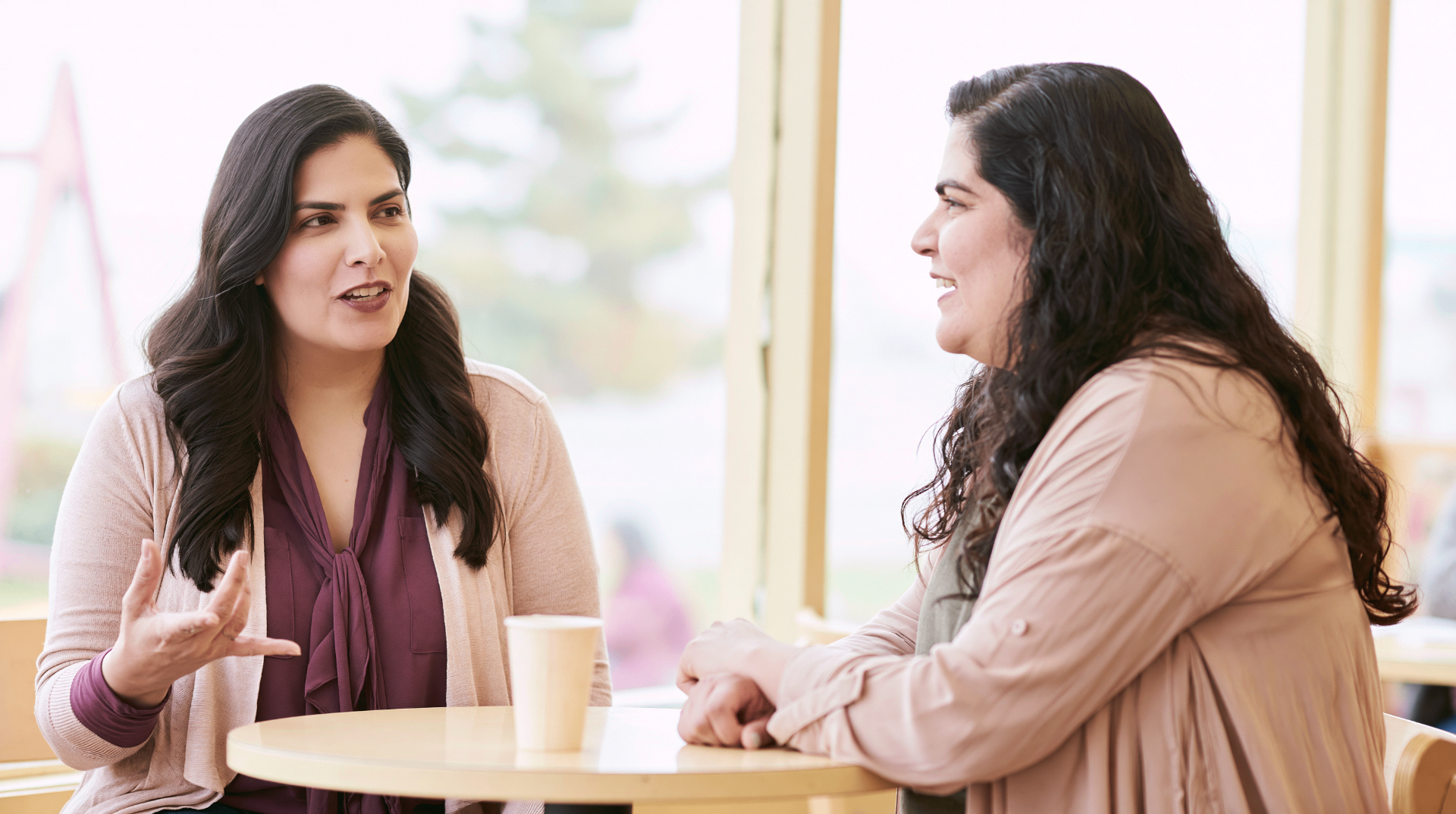 Two adults in genuine, animated conversation at a small cafรฉ table by a window